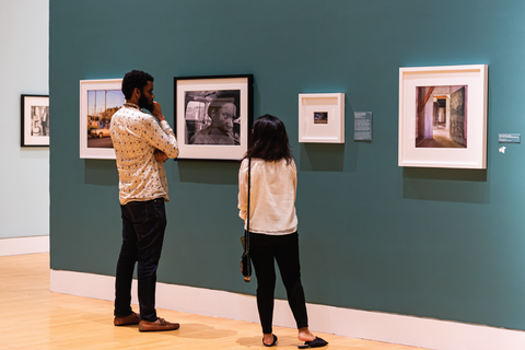 Two people standing in a gallery with four photographs on the wall